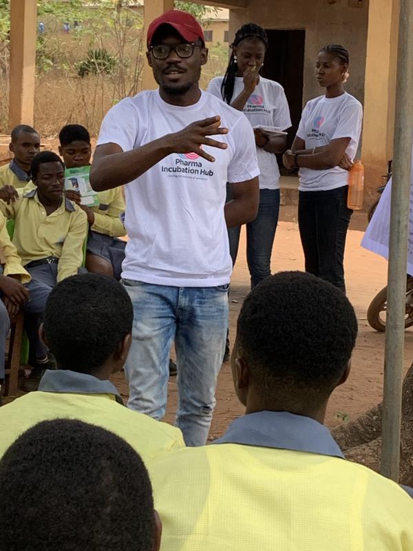 A fellow in a Pharma Incubation Hub shirt speaks to seated students while three teammates stand behind him