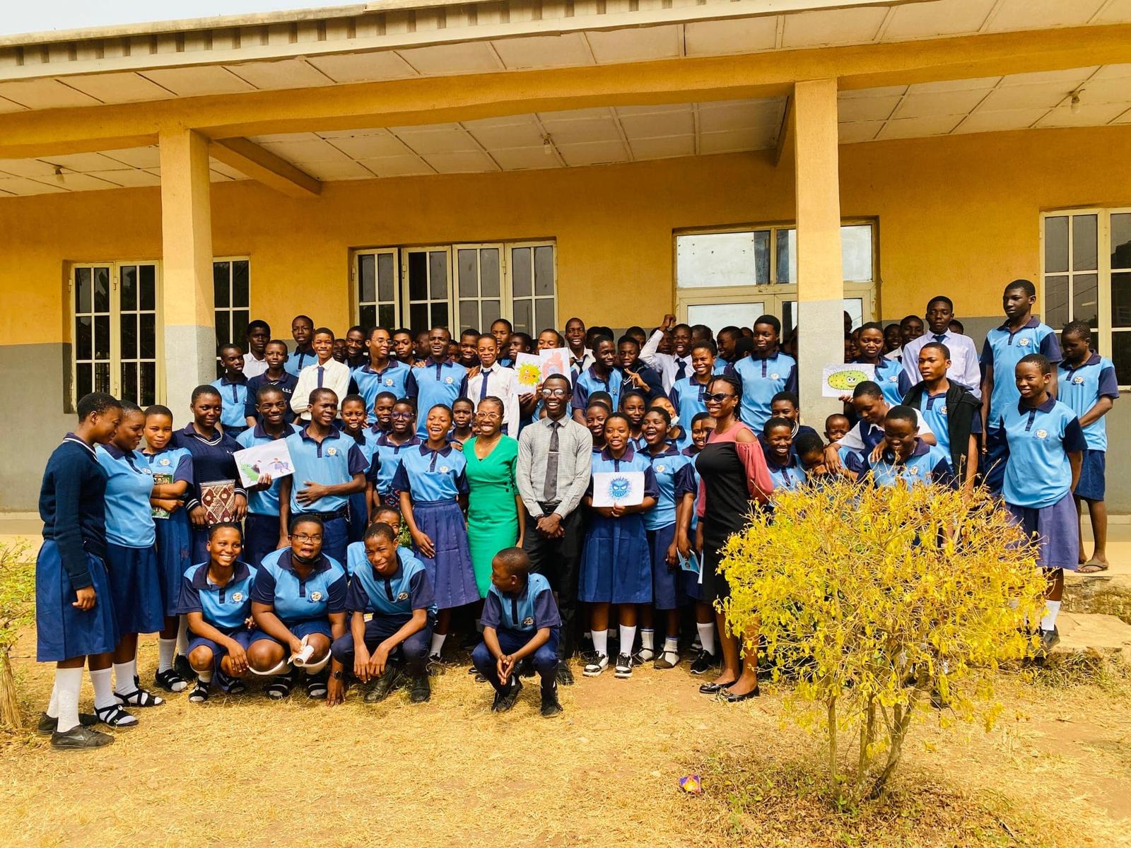 Dozens of secondary school students in blue uniforms pose with fellows and teachers outside their school building